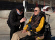 Man met ALS zit in een rolstoel in de zon en wordt geholpen door een andere man