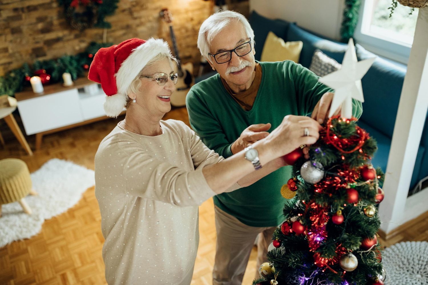 Ouder echtpaar is kerstboom aan het optuigen. Uitkijken dat ze geen verrekte spier krijgen.