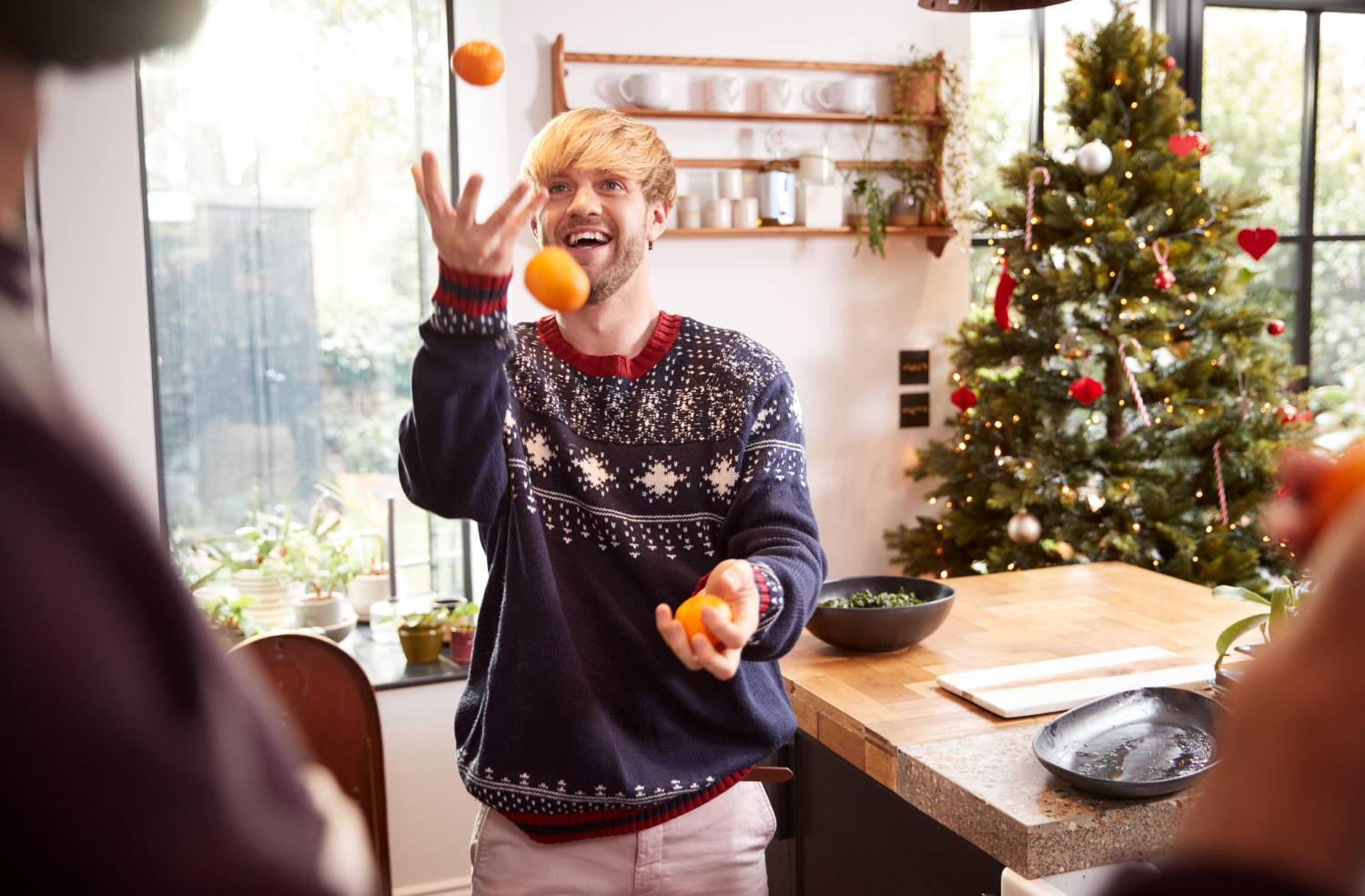 Man in een kerstrui speelt met gezonde kerstcadeaus bij de kerstboom