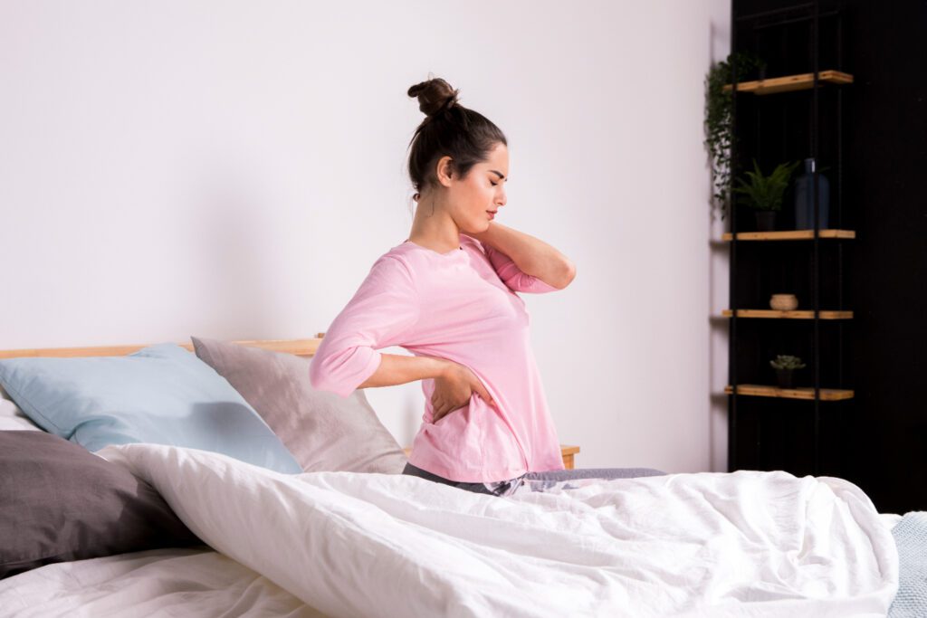 Vrouw in een roze shirt heeft last van ischias en staat niet op na het slapen in haar slaapkamer